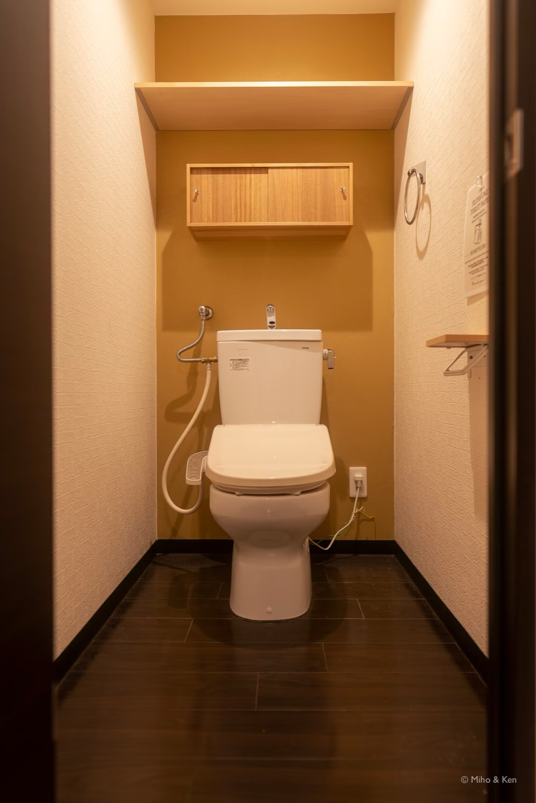 からし色の壁と木の吊り戸棚がある独立したトイレ