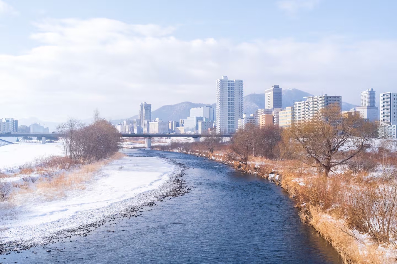 冬の豊平川。雪の河川敷の向こうに札幌の街並みと山が見える